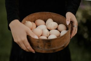 a woman holding a wooden bowl filled with eggs