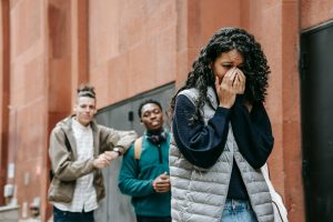 From below of despaired young ethnic female student covering mouth with hands while crying on street after being bullied by multiracial classmates