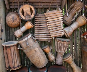 A variety of rustic handmade percussion instruments displayed on a wooden wall.