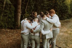 Groomsmen huddle in a supportive circle outdoors, preparing for a wedding ceremony.