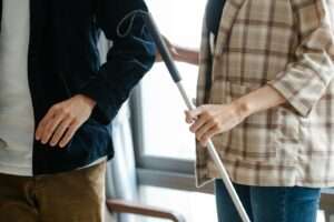 Individuals in casual attire offering support with a walking stick indoors.