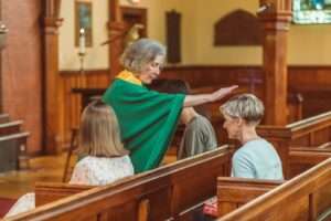 Elderly woman blessing two adults in a church pew, signifying faith and spirituality.