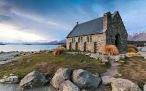 Picturesque stone church by Lake Tekapo with mountains in the background at dusk.