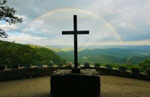 A serene mountain landscape featuring a cross and a beautiful rainbow in the sky.