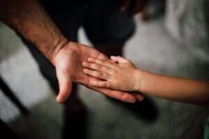 Close-up of a child's hand resting gently on a man's hand, symbolizing love and support.