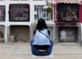 A woman sits in reflection at a columbarium adorned with flowers in Callao, Peru.