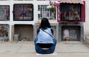 A woman sits in reflection at a columbarium adorned with flowers in Callao, Peru.