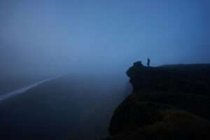 person standing rock cliff covered with fog
