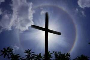 A cross silhouetted against a dramatic sun halo and clouds in India.