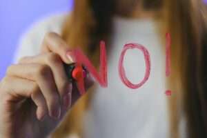 Close-up of teenager writing 'No!' in red on glass, symbolizing refusal, captured in vibrant studio setting.