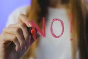 Close-up of teenager writing 'No!' in red on glass, symbolizing refusal, captured in vibrant studio setting.