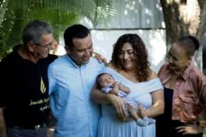Joyful family gathering with proud parents and grandparents holding a newborn baby outdoors.