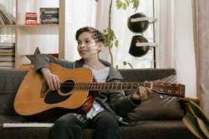 A joyful child playing acoustic guitar on a cozy couch, enjoying his musical hobby.
