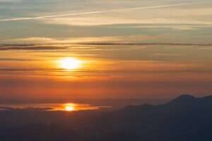 A tranquil sunrise view with vibrant colors reflecting over a mountain range and water.