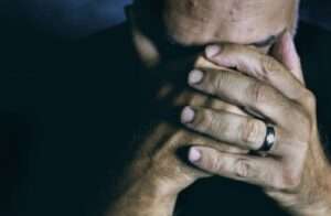 Close-up of an elderly man covering his face, expressing sadness and contemplation.