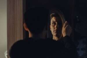 A man gazing at his reflection, capturing an introspective moment indoors.