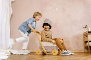 Two children playing with a handmade wooden toy cart indoors, smiling and enjoying themselves.