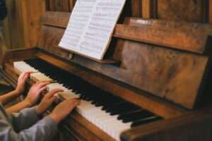 Close-up of children playing a piano with visible sheet music indoors.