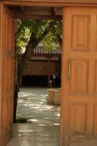 A wooden door opens to reveal a sunlit courtyard with a tree and fountain in Kastamonu, Türkiye.