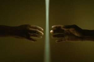 Two hands reaching toward each other through a beam of light, concept of connection and distance.