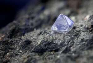 A small purple crystal rests on dark rock