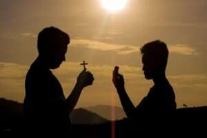 Two men silhouetted against a sunset sky, one holding a cross, symbolizing faith and spirituality.
