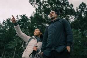 Two hikers enjoy an outdoor adventure exploring a lush nature trail, pointing towards distant sights.