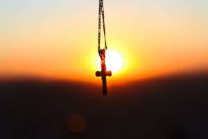 A cross pendant silhouetted against a vibrant sunset, symbolizing faith and peace.