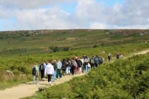 A group of people walking along a dirt path through a green moorland